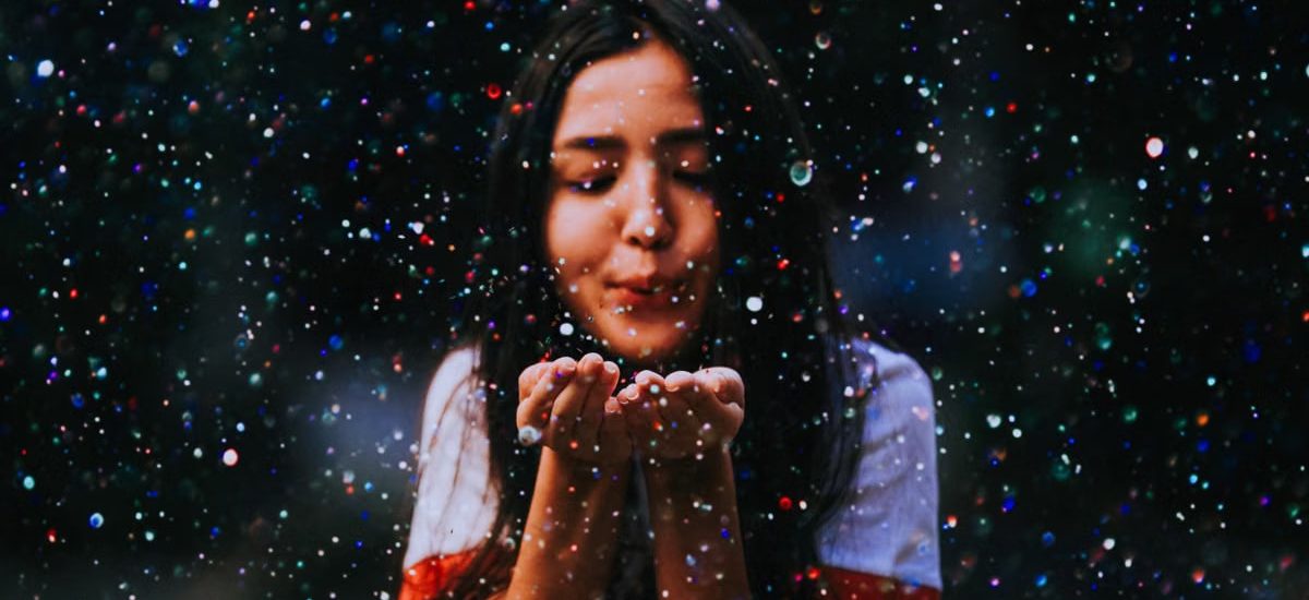 Joyful teenage girl blows vibrant particles, creating a magical atmosphere